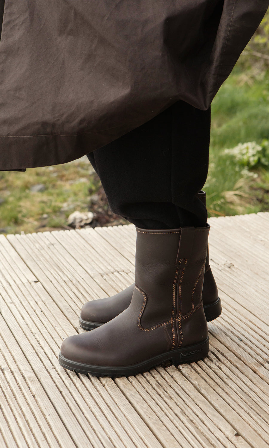 Plümo  Person in Rigger Boots with cushioned removable sole stands on a wooden deck; brown leather and stitching show.