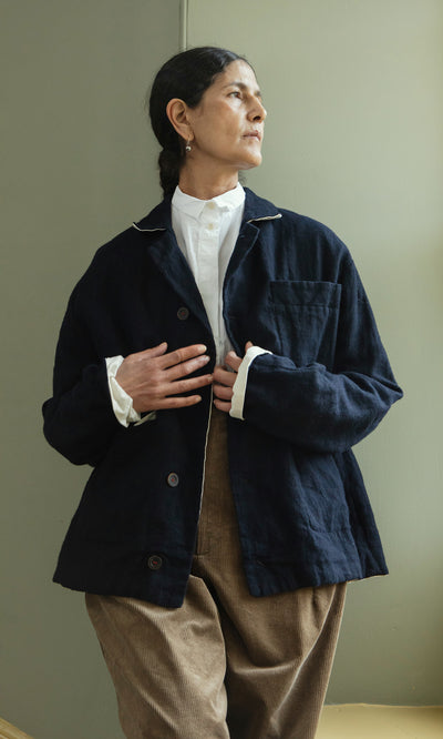 Plümo  Individual in a Dunbar Tweed Jacket and brown pants stands by a green wall, gazing sideways with hand on chest.