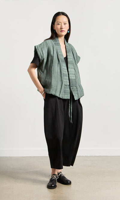 Plümo- Woman in a loose Fawn Gilet, black top, and pants stands confidently against a plain light background.