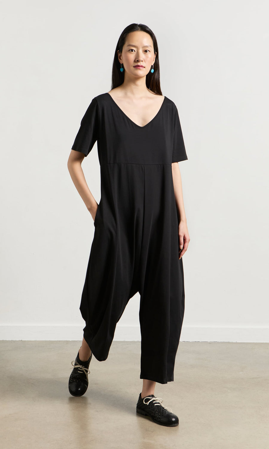 Plümo- Woman in Fenzi Jumpsuit—an oversized black, short-sleeve style—paired with black shoes and blue earrings.