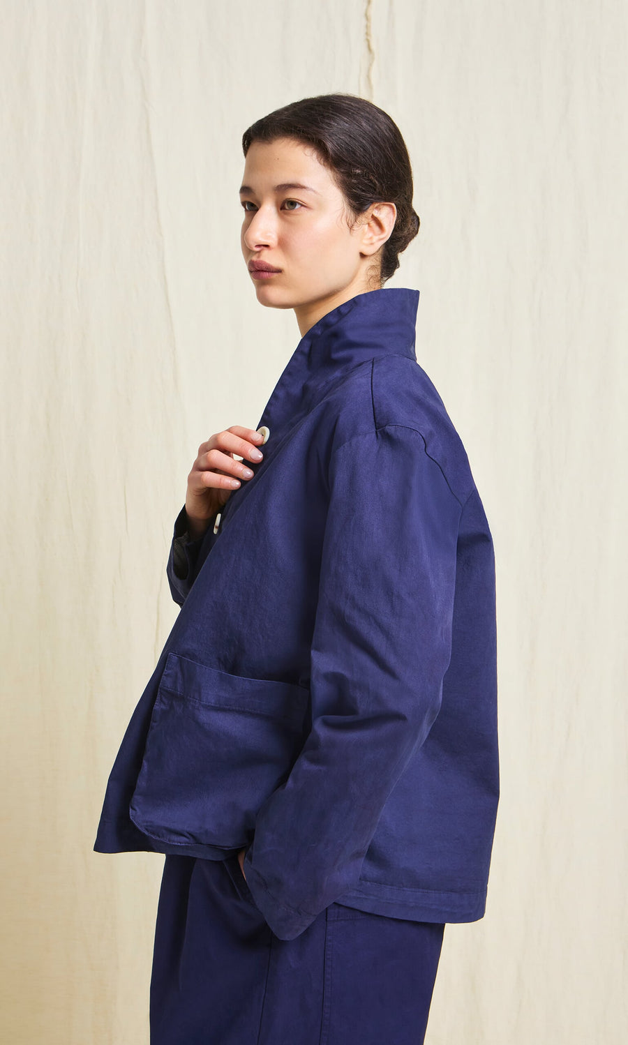 Plümo- A person in the Gardener's Jacket - Navy stands sideways, one hand touching the jacket collar.