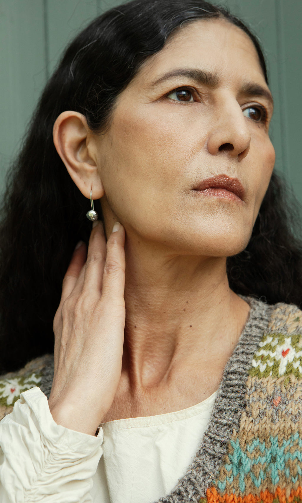 Plümo  Woman with long dark hair in a knit vest and Greta Earrings - Silver looks thoughtfully to the side.