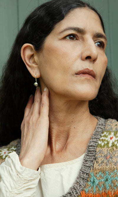Plümo  Woman with long dark hair in a knit vest and Greta Earrings - Silver looks thoughtfully to the side.