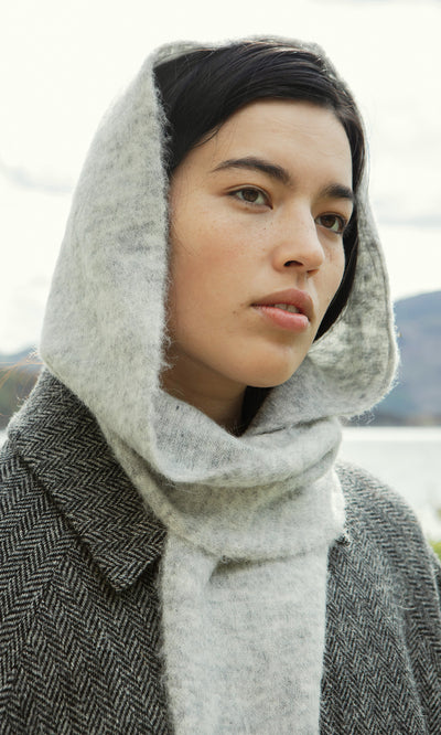 Plümo  Woman in a Grey Bonnet and wool coat, showcasing Danish design, gazes thoughtfully into the distance outdoors.