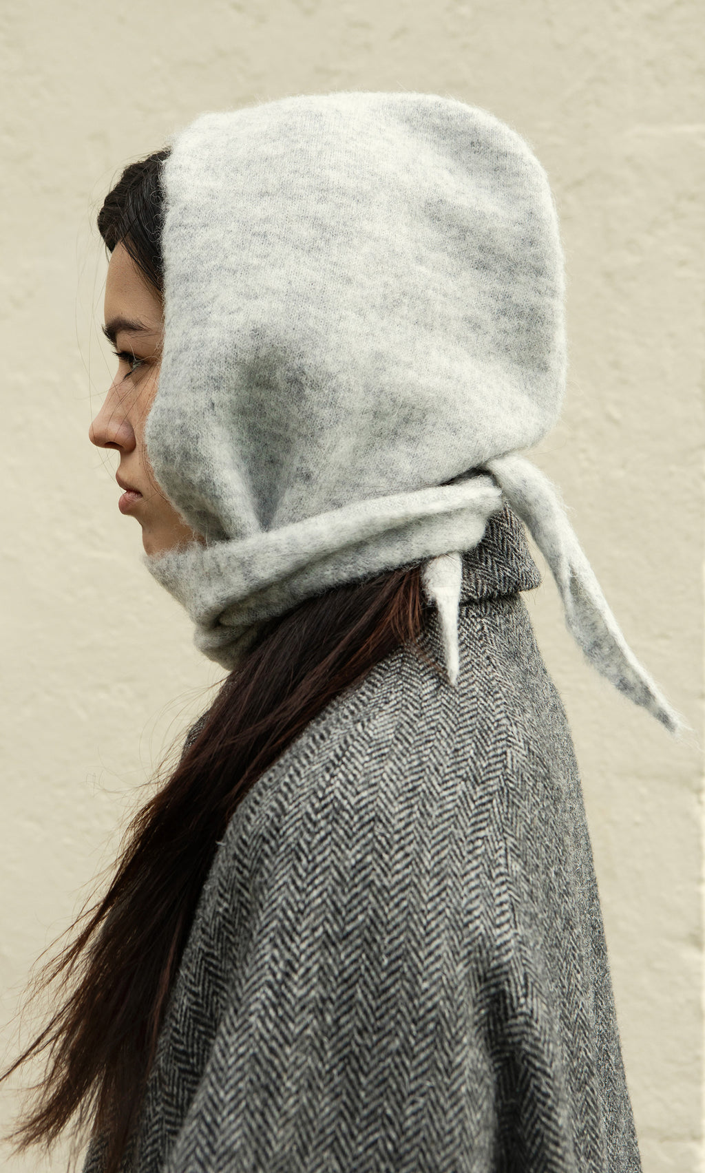 Plümo  Person in profile wears the Grey Bonnet, a Danish-designed woolen hood, standing against a plain light wall.
