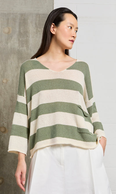 Plümo- Woman in the Hagen Stripe Jumper, a relaxed fit V-neck with sage and white stripes, paired with white pants.