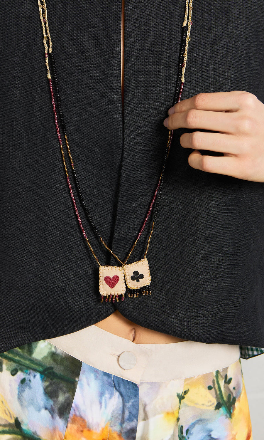Plümo- A person wears a black top, floral pants, and the Hearts & Clubs Necklace.