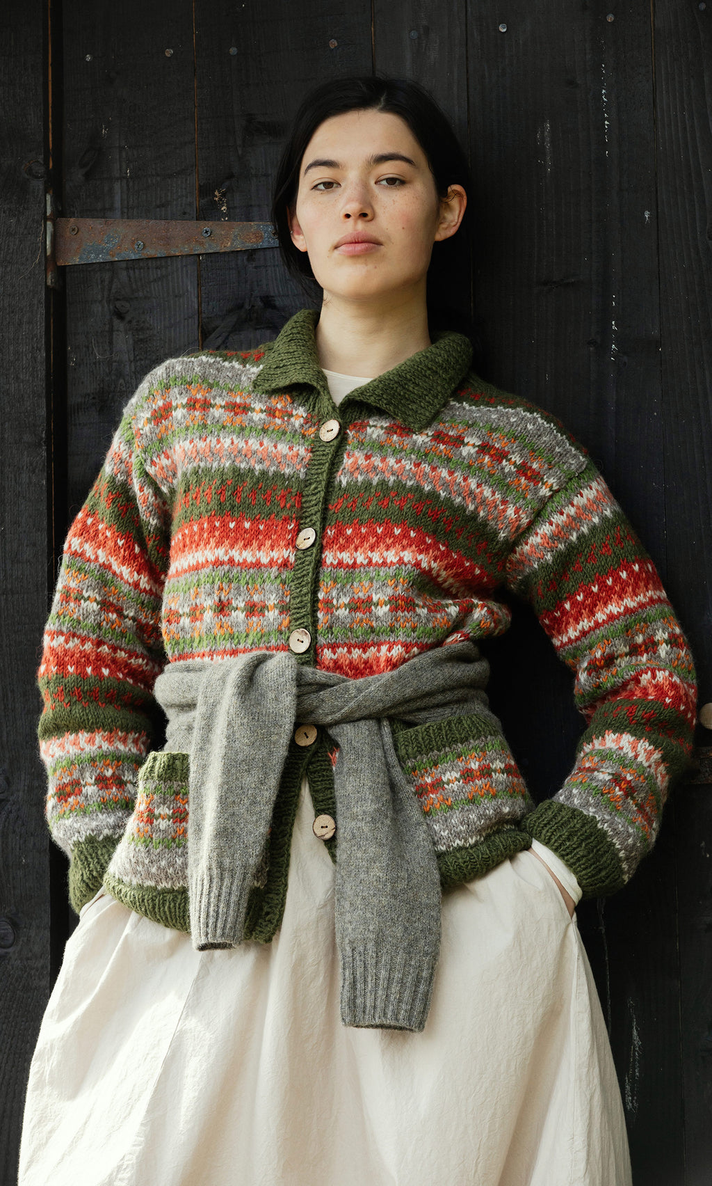 Plümo  Person wears a Hebrides Cardigan against a dark wood background, looking at the camera.