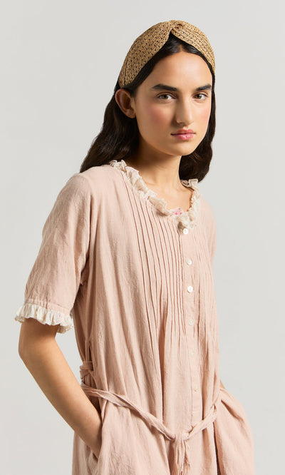 Plümo- Woman wearing the Heide Dress in pink ticking stripe with white buttons and a tan woven headband, against a neutral background.
