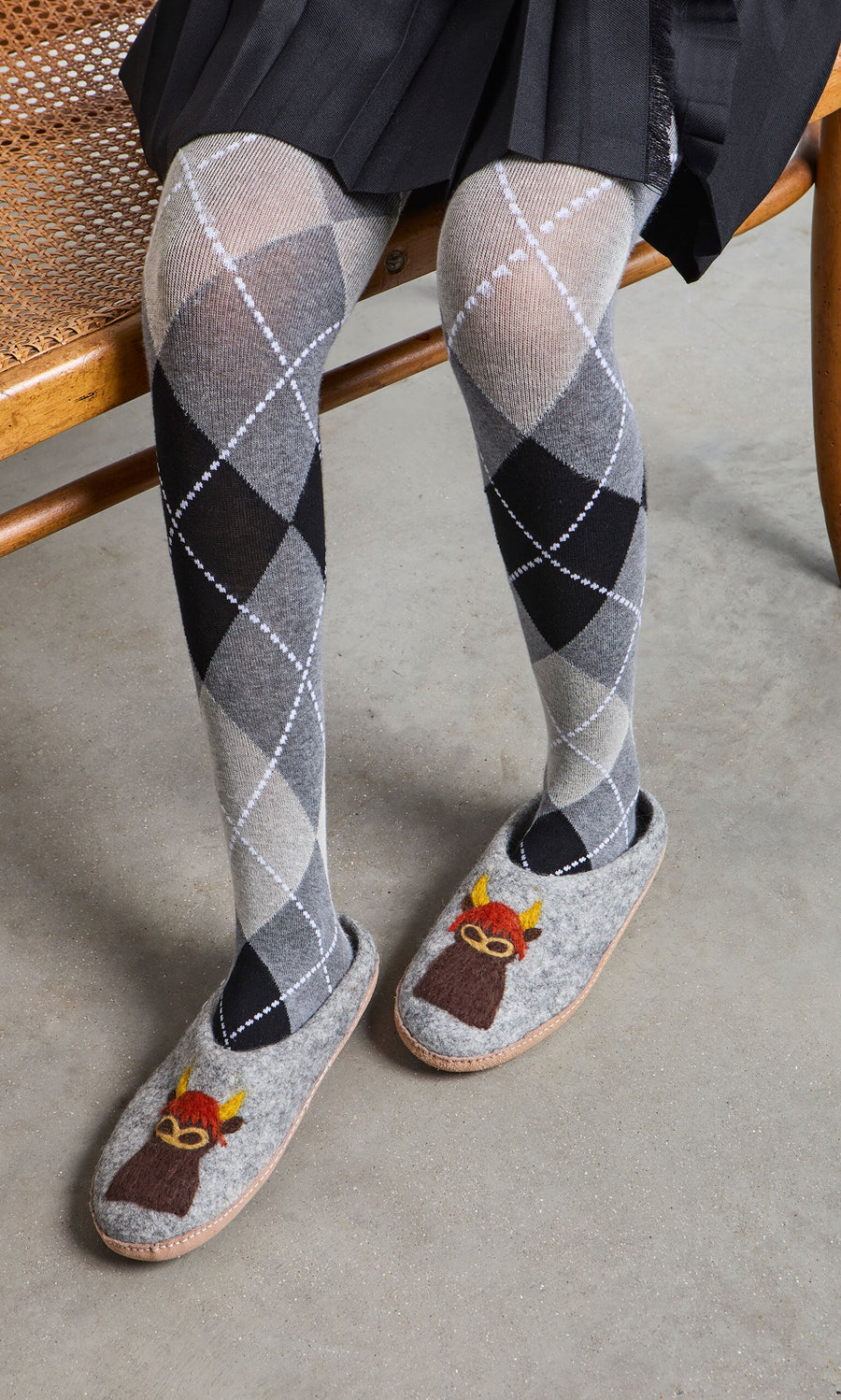 Plümo- Person wearing gray argyle tights and Highland Slippers, sitting on a wooden bench.