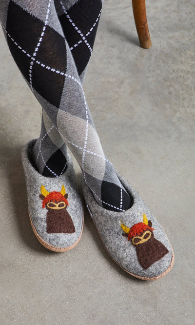 Plümo- Person wearing gray argyle tights and Highland Slippers with horns and red hair, sitting on a chair.