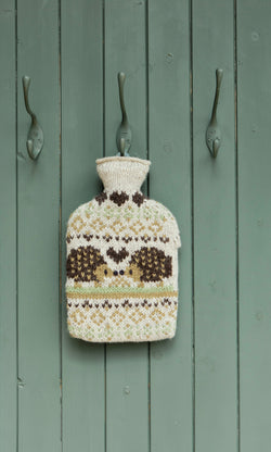 Plümo  The Hedgehog HWB hangs on a green door between three metal hooks, showcasing its hand-knitted patterned design.