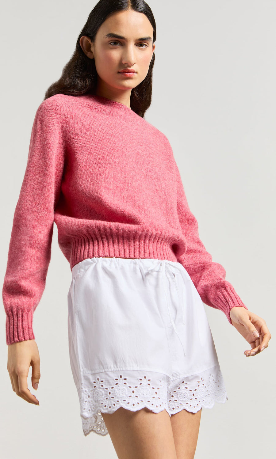 Plümo- Woman wearing a pink sweater and relaxed fit Hurlingham Shorts, standing against a light background.