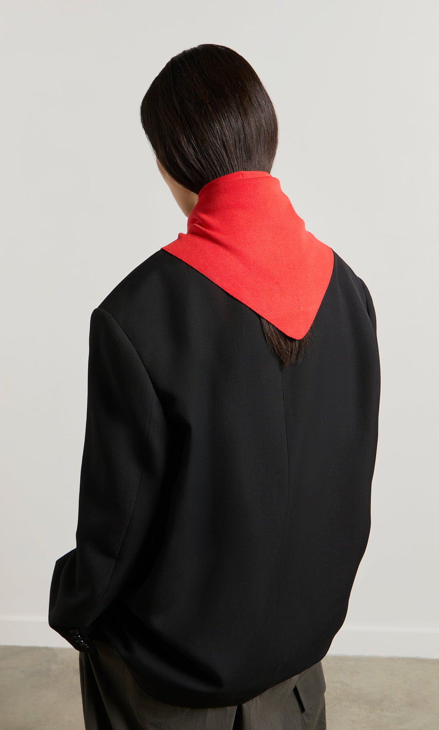 Plümo- Person with dark hair in a black blazer, wearing the Jona Necktie - Lava over their shoulders, facing away.