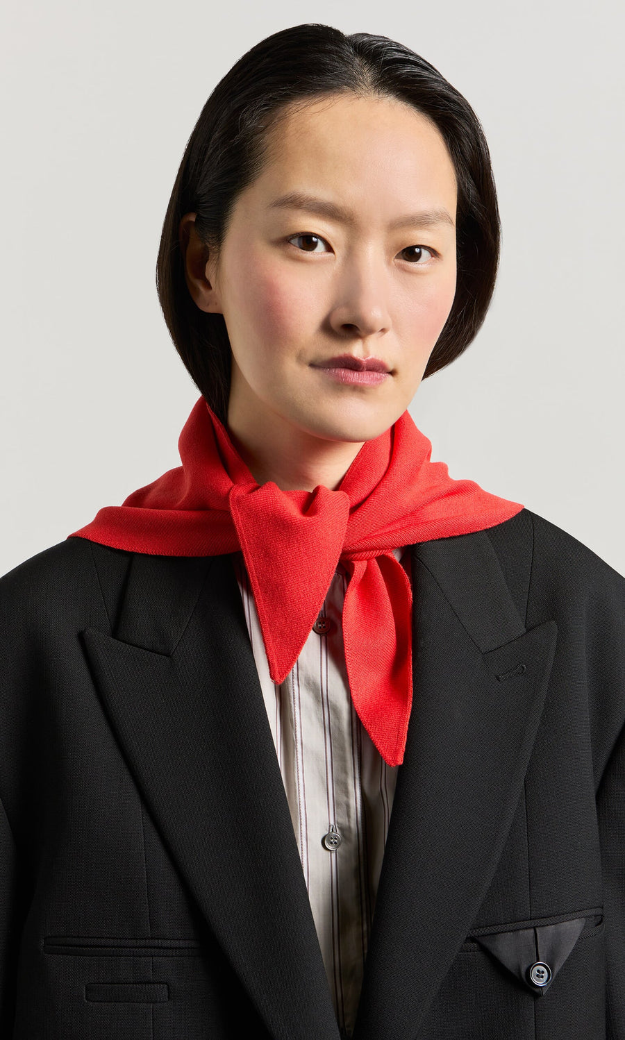 Plümo- Person with short dark hair in a black blazer, striped shirt, and the Jona Necktie - Lava around their neck.