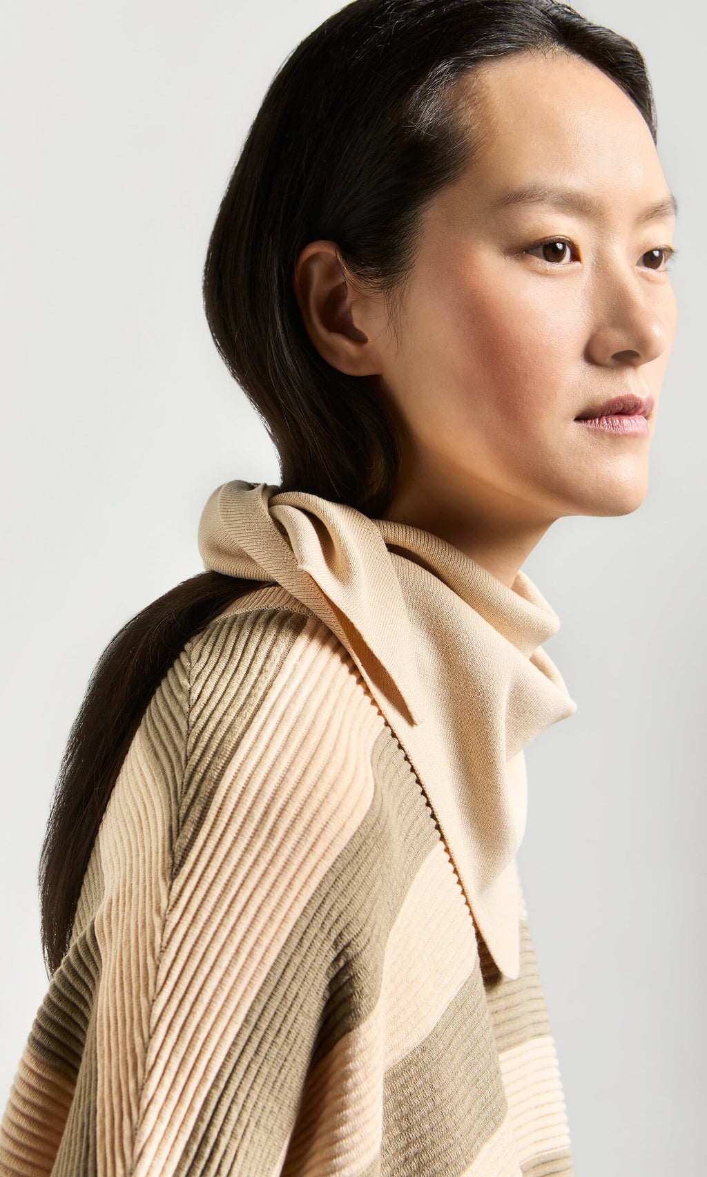 Plümo- A woman in a supersoft, beige Jona Necktie - Silt gazes to the side against a light background.