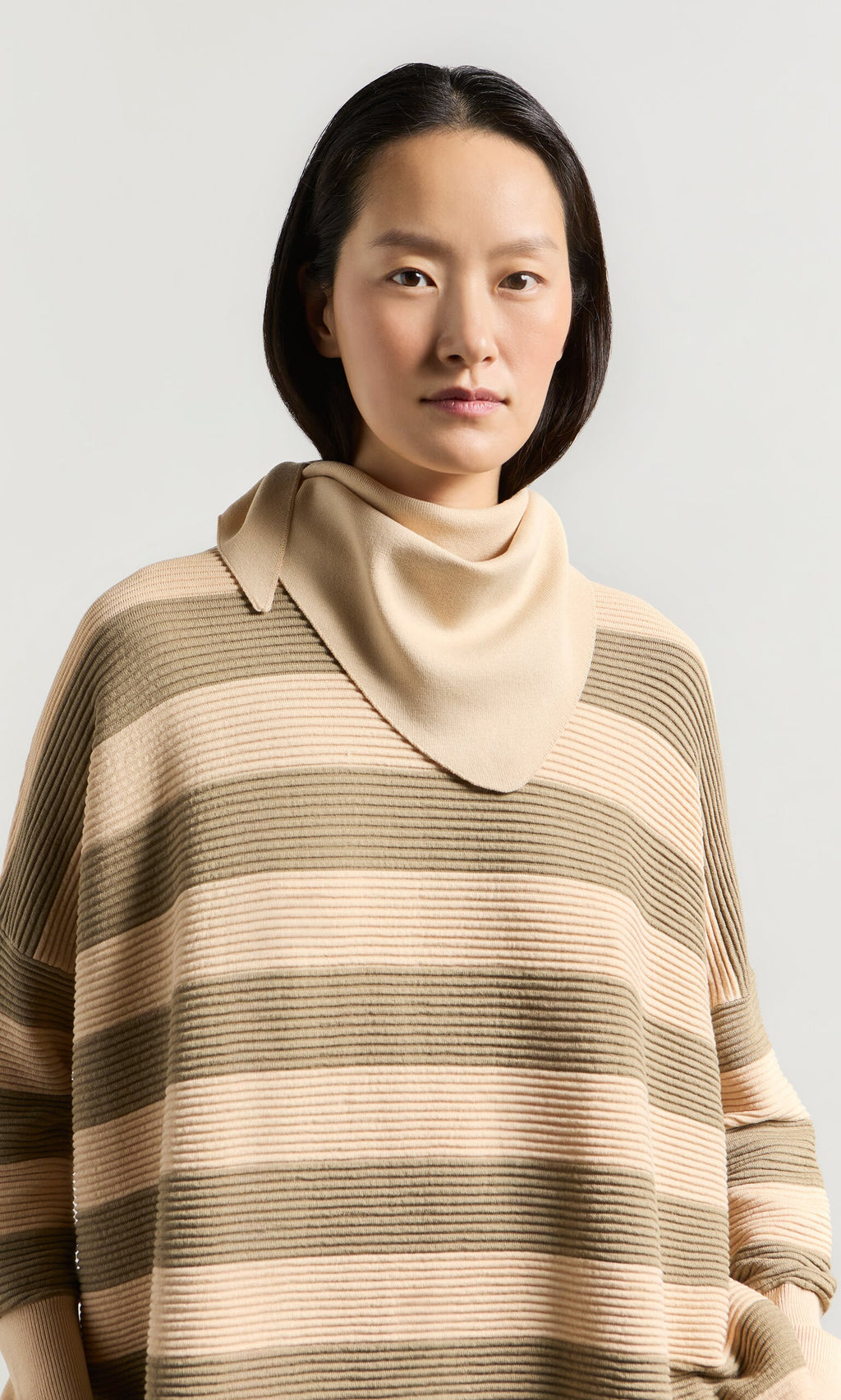 Plümo- Woman with straight dark hair in a Jack Sweater - Silt and beige scarf, standing against a light background.