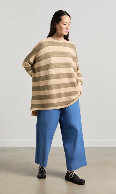 Plümo- Woman in the Jack Sweater - Silt by Plümo Studio and wide blue pants stands against a light background, looking sideways.