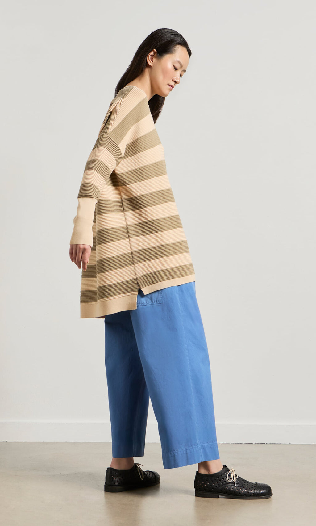 Plümo- Woman in a relaxed Jack Sweater - Silt and blue wide-leg pants stands sideways against a plain light background.