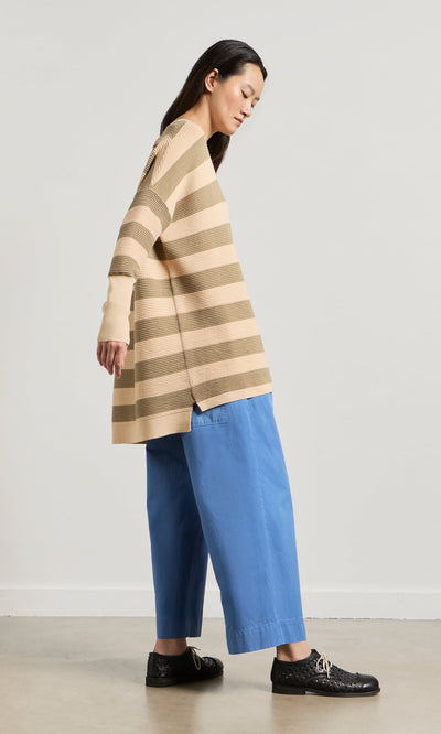 Plümo- Woman in a relaxed Jack Sweater - Silt and blue wide-leg pants stands sideways against a plain light background.
