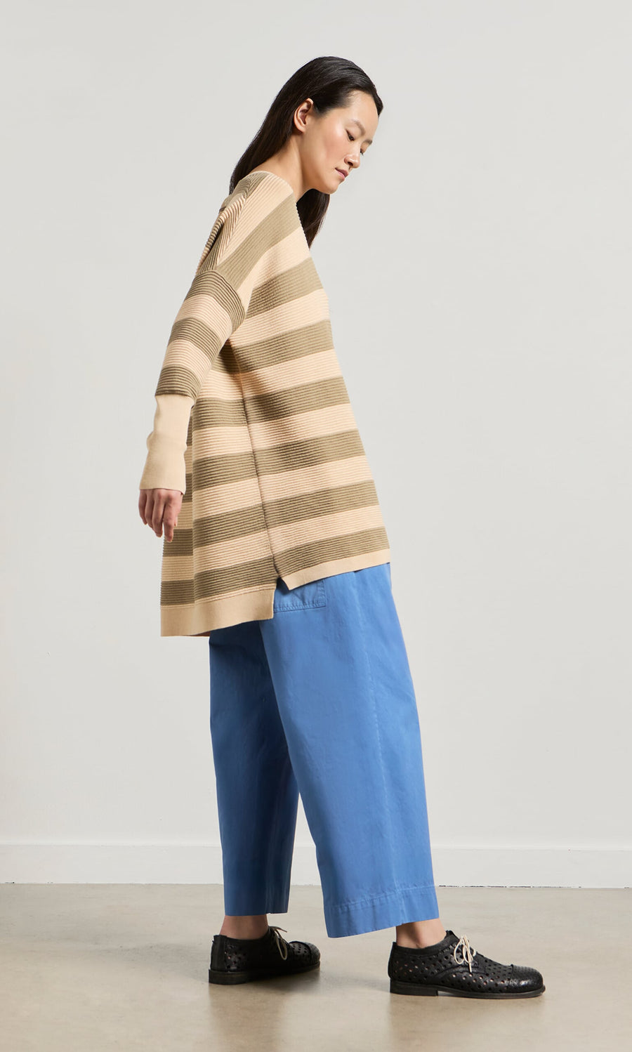 Plümo- Woman in a relaxed Jack Sweater - Silt and blue wide-leg pants stands sideways against a plain light background.
