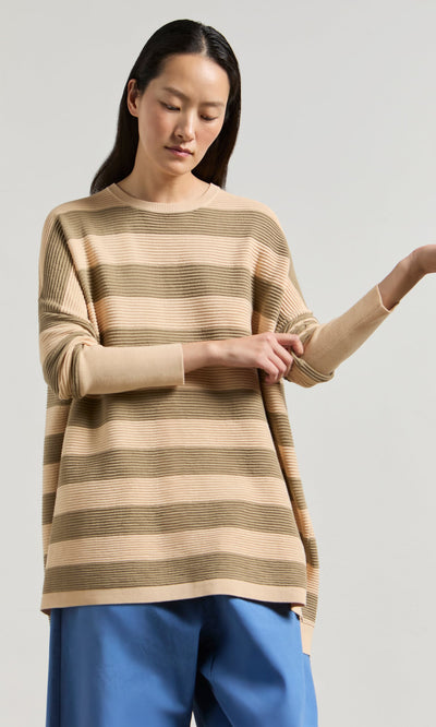 Plümo- Woman in the Jack Sweater - Silt by Plümo Studio rolls up her sleeve against a light background.