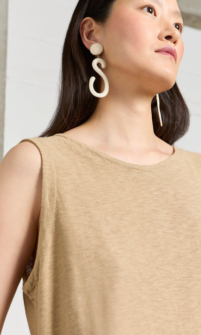 Plümo- Woman in a sleeveless beige top wearing Horn Clip-On Earrings, one S-shaped, gazing off to the side.