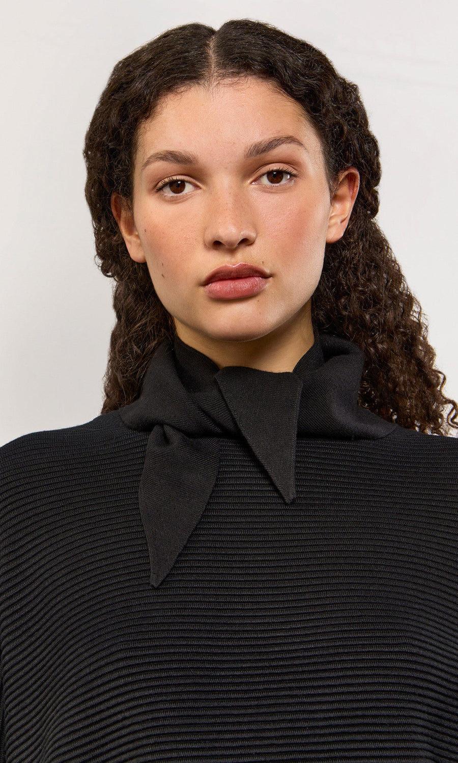 Plümo- Woman with curly hair in a black ribbed top and Jona Necktie - Black, facing forward against a light background.