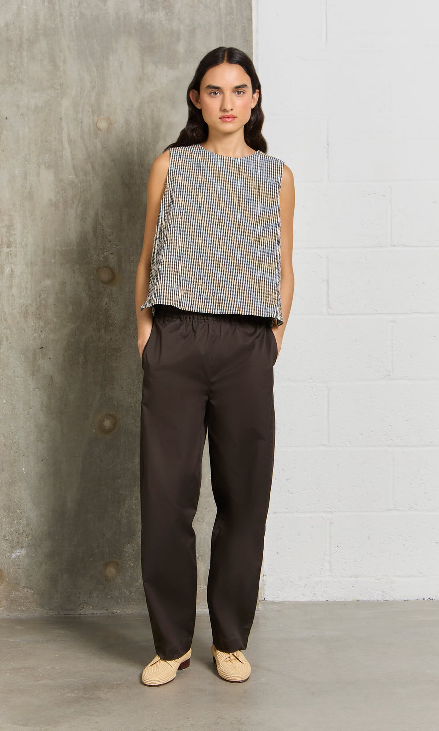 Plümo- Woman standing by a concrete wall in a sleeveless patterned top and Kathleen Pants with a drawstring waist.