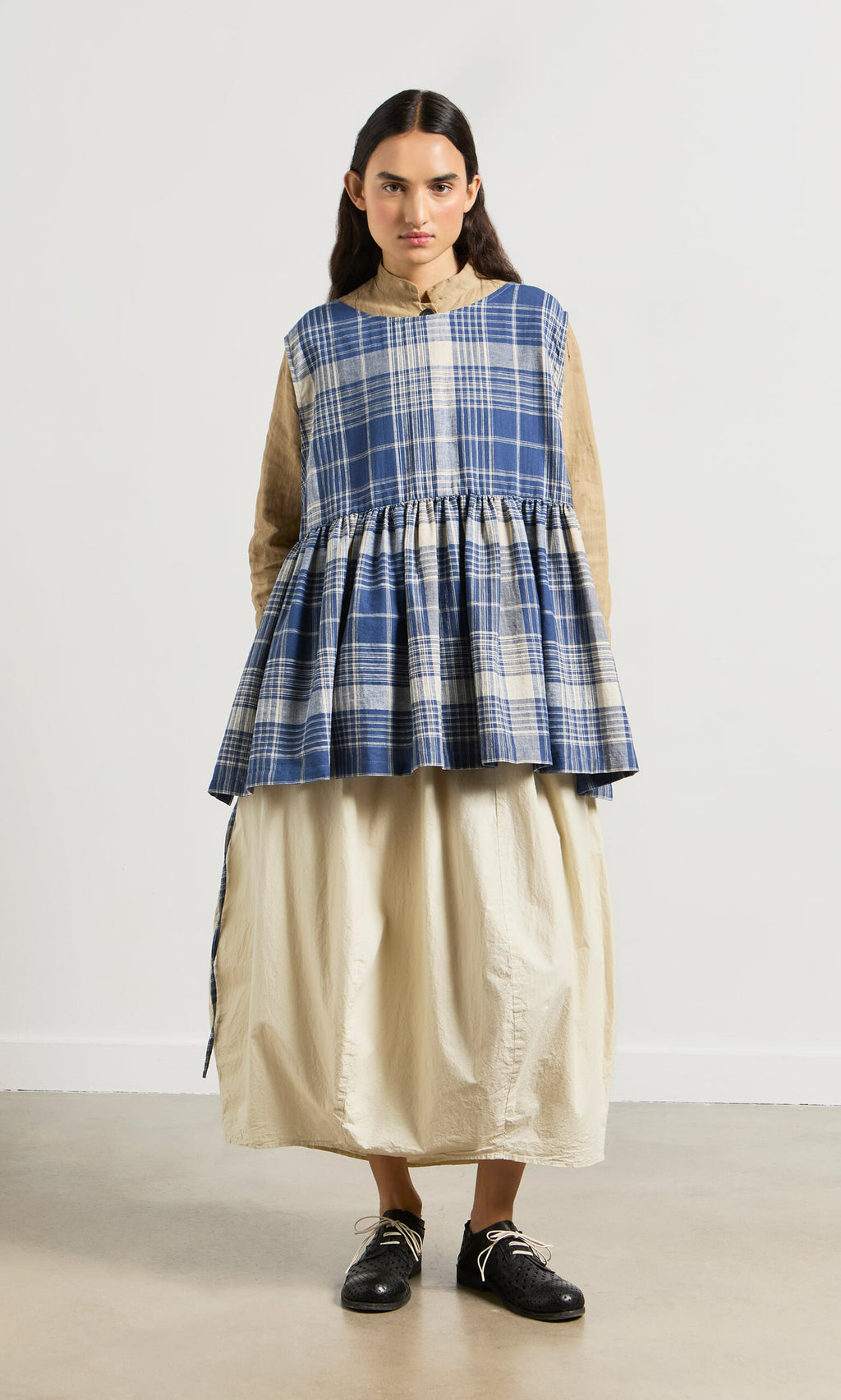 Plümo- Woman wearing a blue Keefe Tabbard made from Japanese Banshu-ori fabric over a beige blouse and cream skirt.