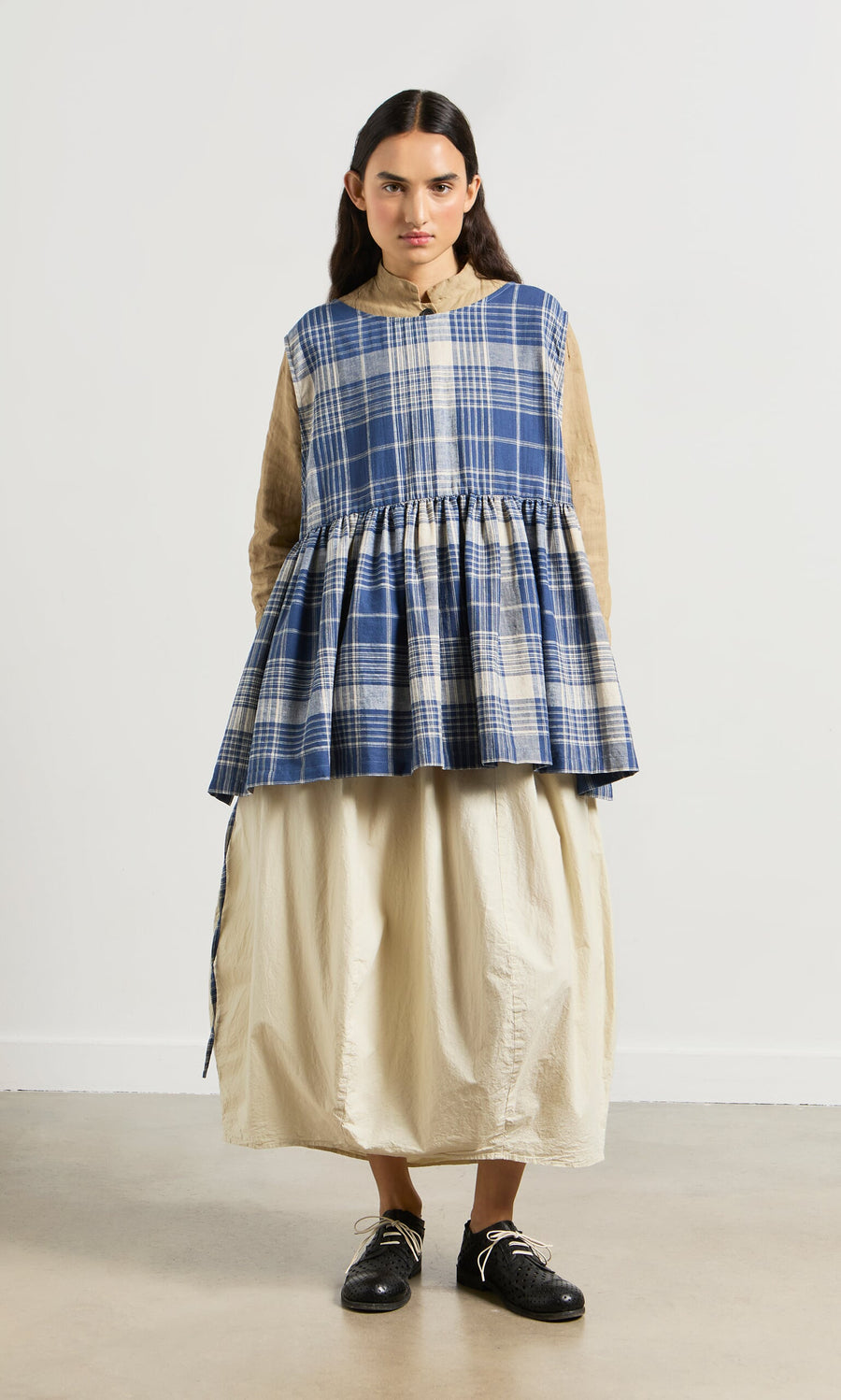 Plümo- Woman wearing a blue Keefe Tabbard made from Japanese Banshu-ori fabric over a beige blouse and cream skirt.