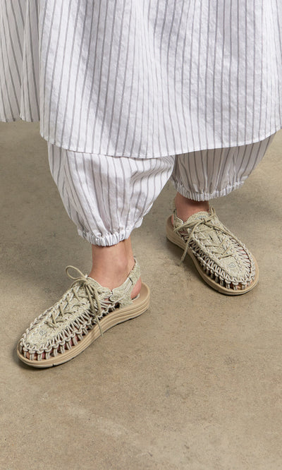 Plümo- Person wearing loose white striped pants and Keen Sandals - Pebble, standing on a concrete floor.