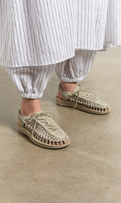 Plümo- Person wearing striped pants, a skirt, and comfy Keen Sandals - Pebble stands on a concrete floor.