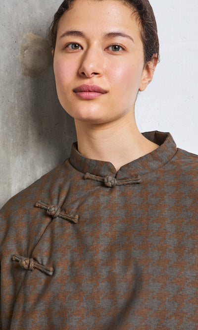 Plümo- Person with short hair wears the Kenza Padded Top, standing by a textured wall.