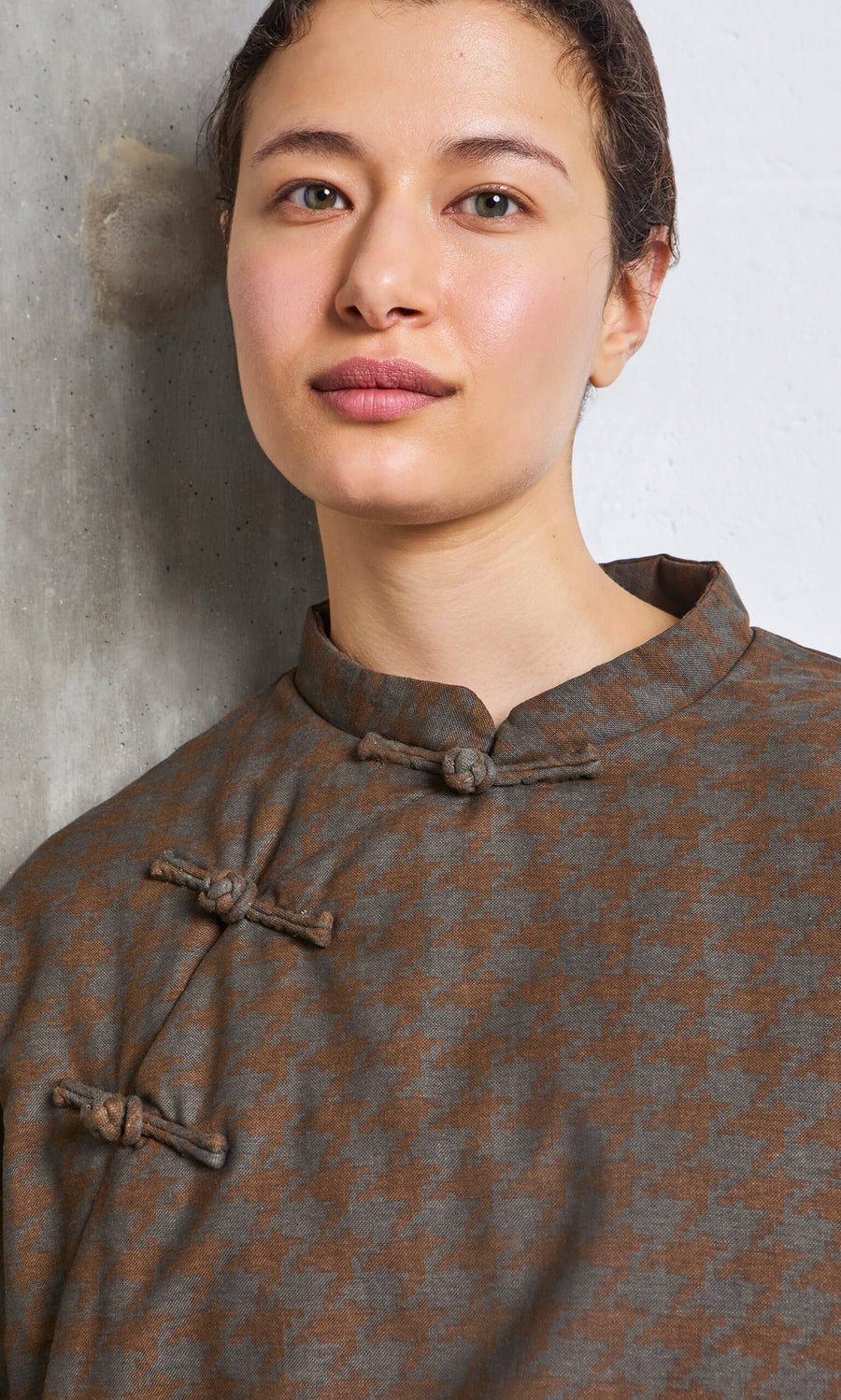 Plümo- Person with short hair wears the Kenza Padded Top, standing by a textured wall.