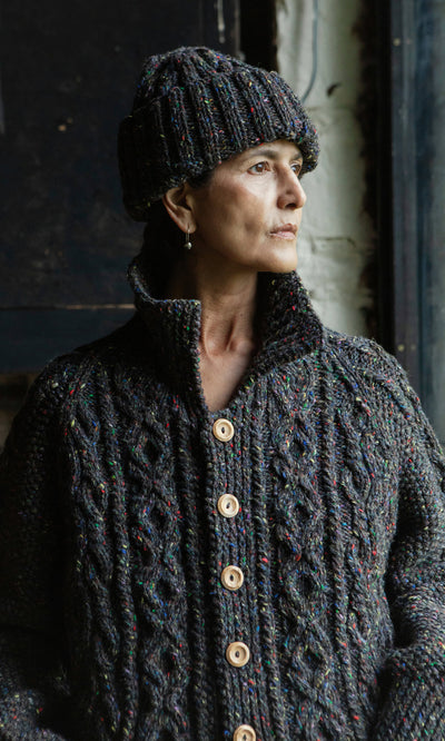 Plümo  Woman in a millstone grey Kilcarra Tweed Cardigan with wooden buttons, gazing out a window to her right.