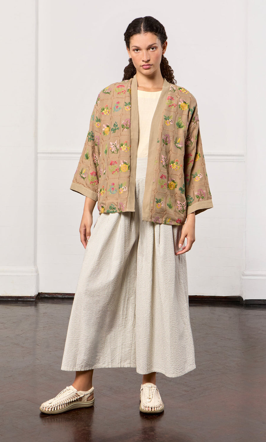 Plümo- Woman wearing a tan floral embroidered jacket, cream shirt, and Laurel Pants stands against a plain background.