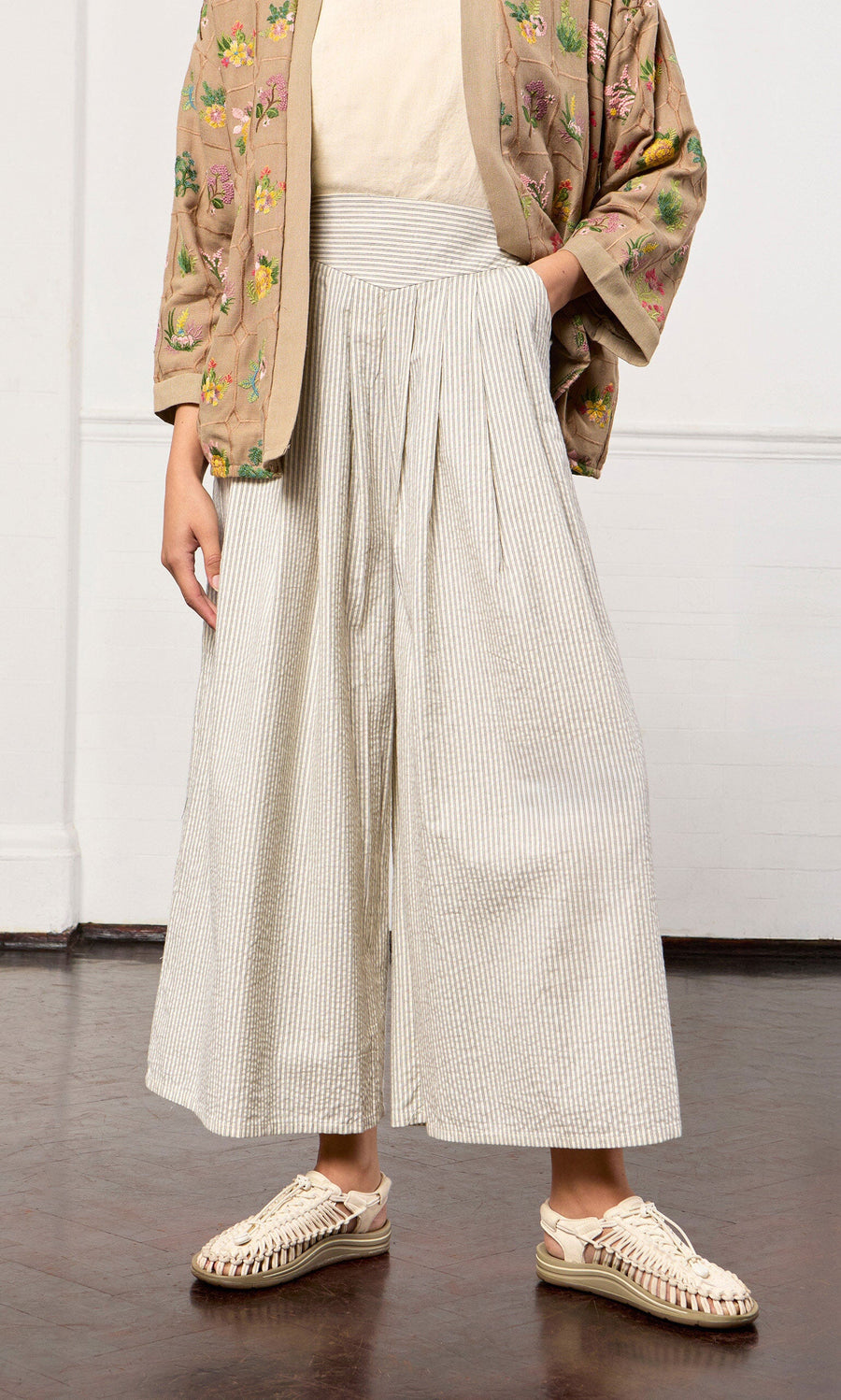 Plümo- Person wearing a floral jacket, cream top, Laurel Pants, and beige woven shoes.