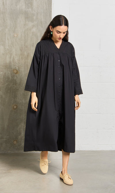 Plümo- Woman wearing the Lily Dress, a vintage black lace long sleeve dress, paired with beige shoes on a concrete floor.