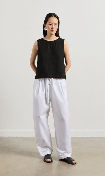 Plümo- Woman in the Linda Top - Solid Black, white wide-leg pants, and statement earrings stands against a plain background.