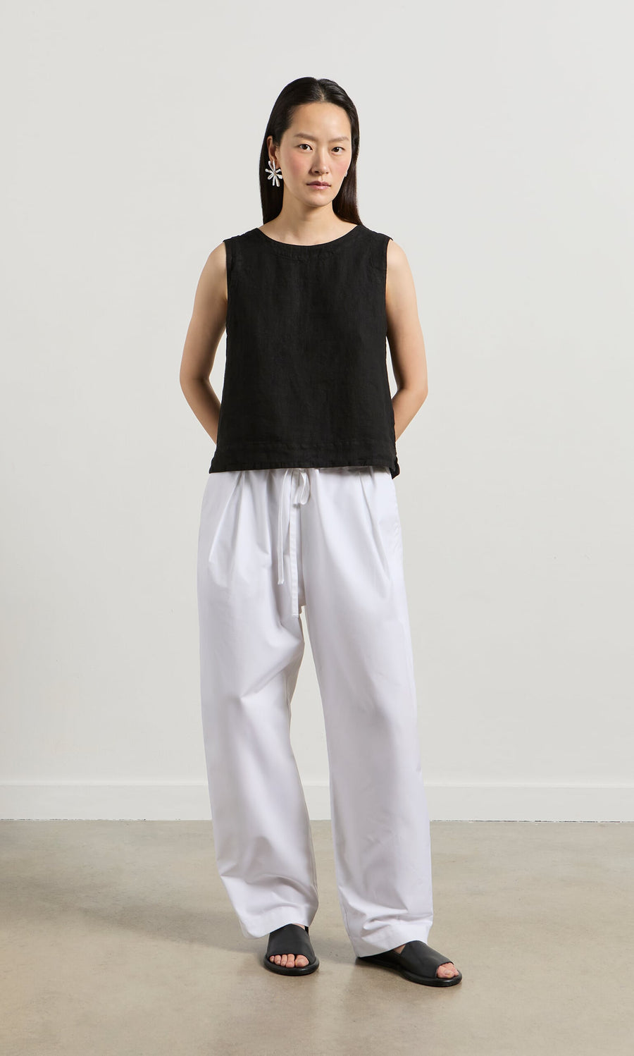 Plümo- Woman in the Linda Top - Solid Black, white wide-leg pants, and statement earrings stands against a plain background.