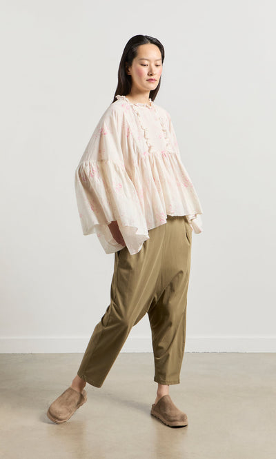 Plümo- Woman in a Litchen Blouse with vintage floral print, khaki pants, and brown slippers stands against a white background.
