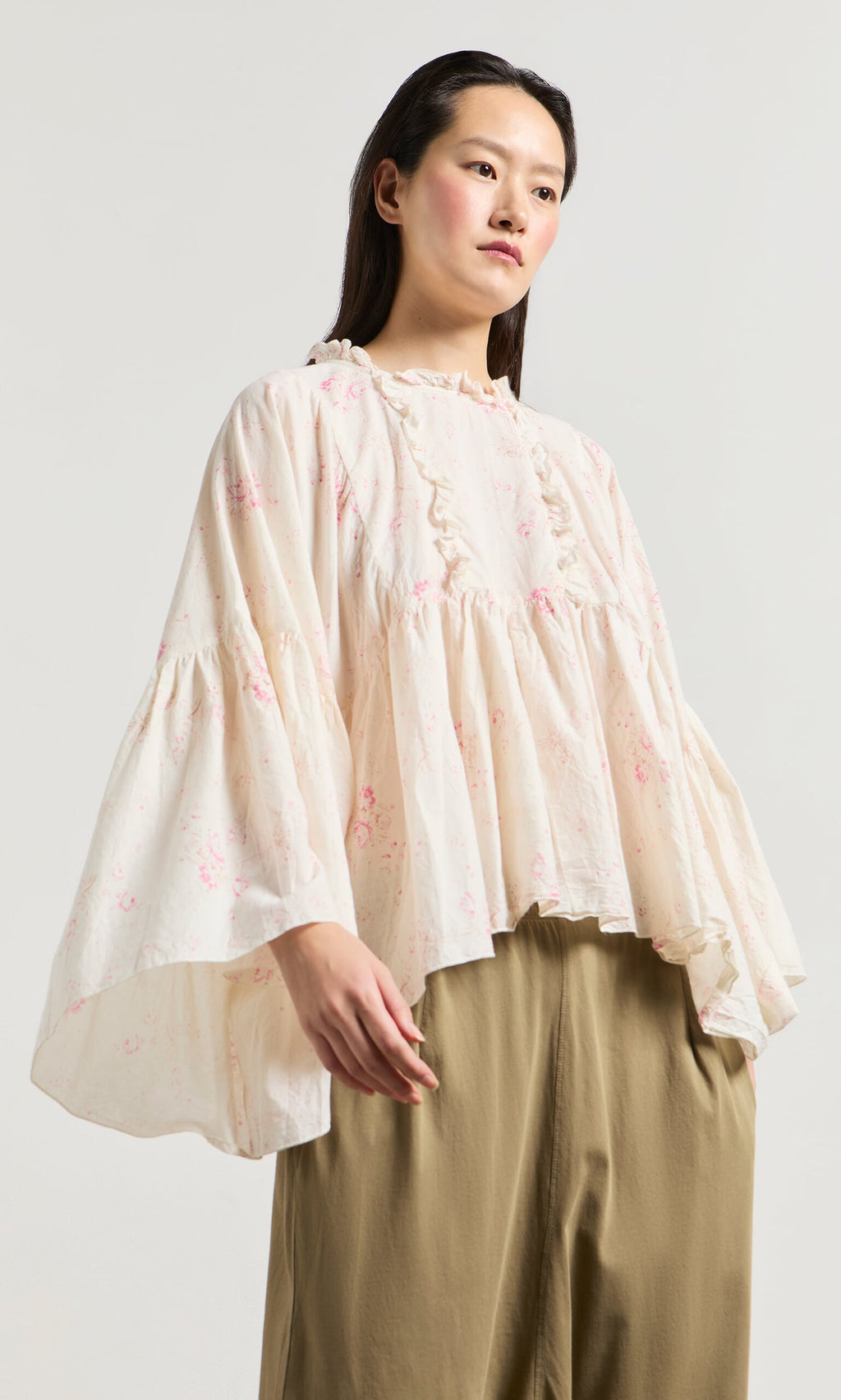 Plümo- Woman wears the Litchen Blouse, a vintage floral print top with ruffled details and wide sleeves, plus tan pants.