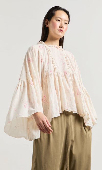 Plümo- Woman wears the Litchen Blouse, a vintage floral print top with ruffled details and wide sleeves, plus tan pants.