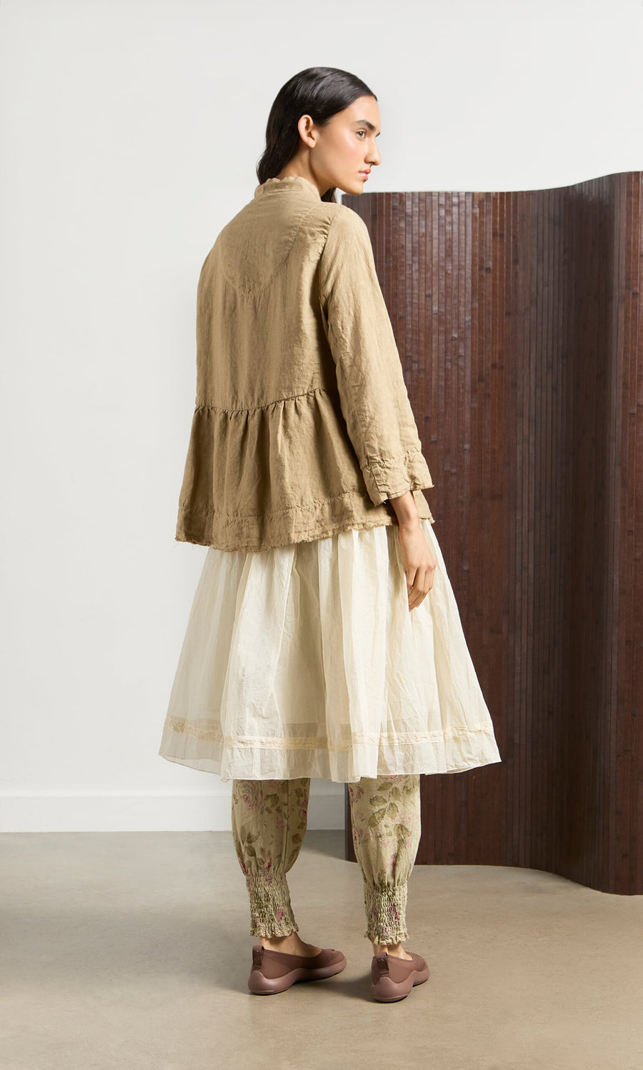 Plümo- Woman in vintage style wearing a beige jacket, Lou Organza Skirt, floral leggings, and brown flats standing sideways.