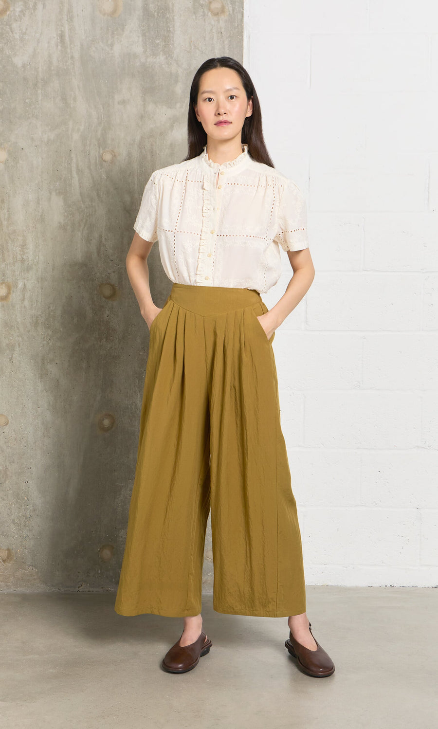 Plümo- Woman stands indoors, hands in pockets, wearing the Gill Blouse and mustard wide-leg pants, facing forward.