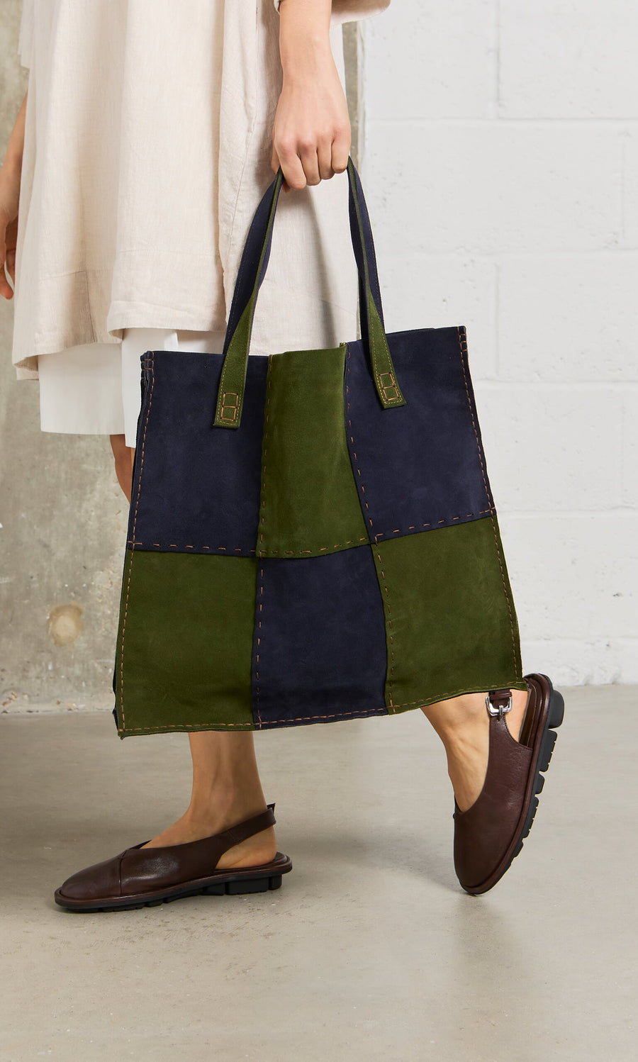Plümo- Person holding a Patchwork Suede Bag with contrast stitching, styled with brown shoes and a cream dress.