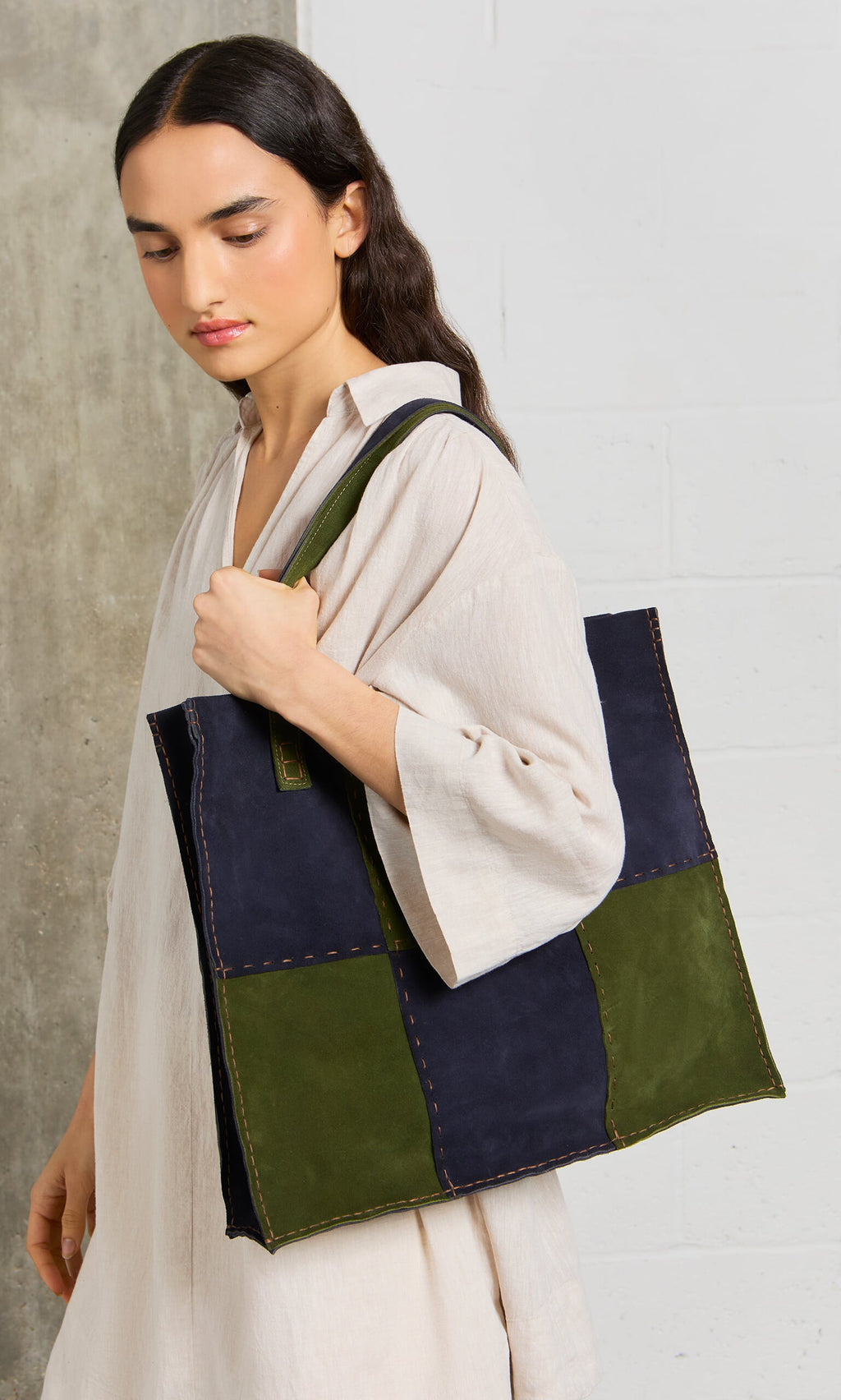 Plümo- Woman in a cream dress carries the Patchwork Suede Bag, a large navy and green tote with contrast stitching.