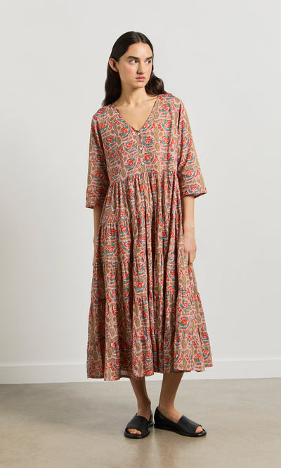 Plümo- Woman in the Nila Flower Dress, a block-printed midi with three-quarter sleeves, and black slide sandals indoors.