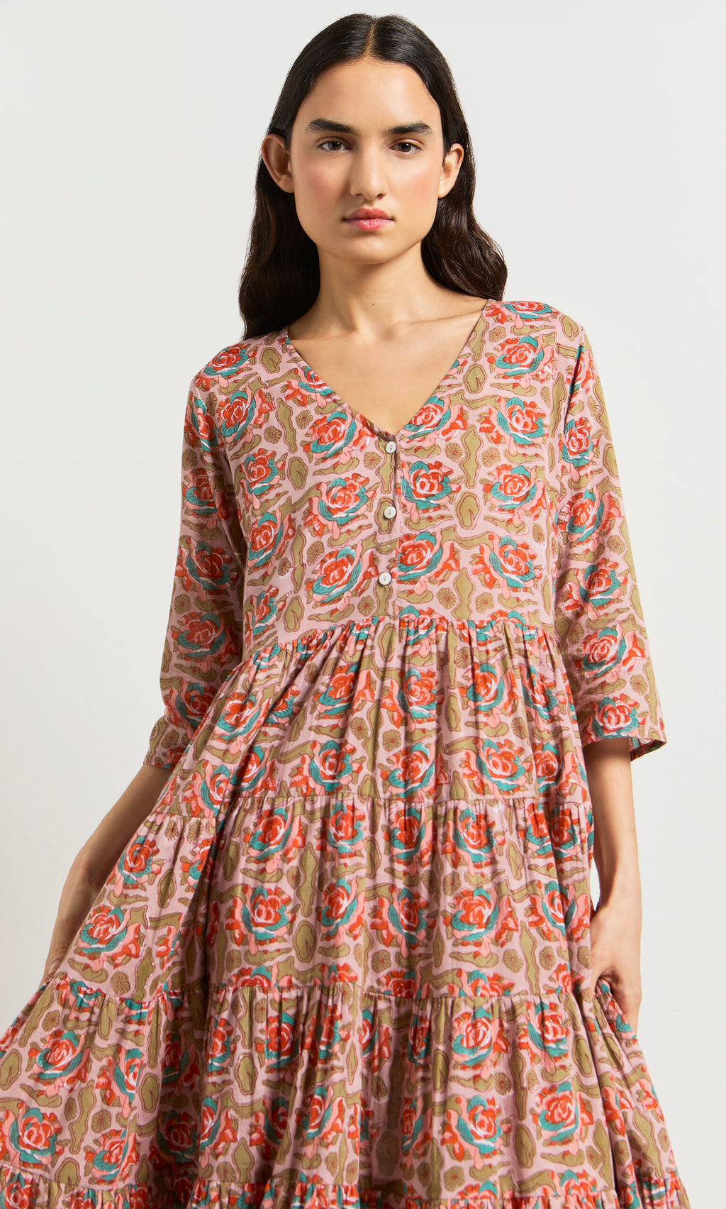 Plümo- Woman wearing the Nila Flower Dress, a block-printed floral midi in pink, red, and green on a beige background.